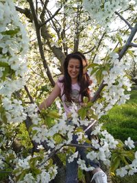 Portrait of smiling young woman against white flowering tree