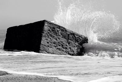 Wave splashing on rock at beach against sky