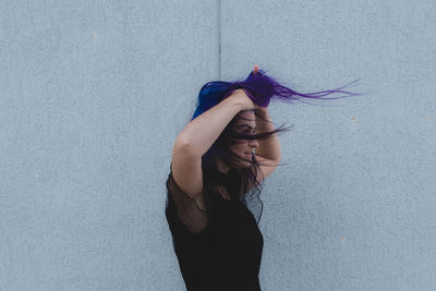 Smiling woman with dyed hair standing against wall