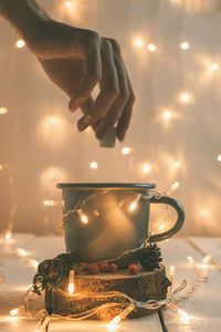 A female hand on the background of new year garland puts sugar in a mug with hot sea buckthorn tea