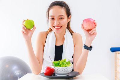 Portrait of woman holding apple against white background