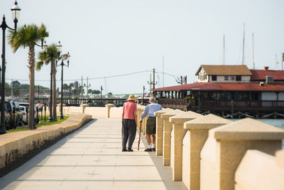 Rear view of senior couple walking on pathway against sky during sunny day