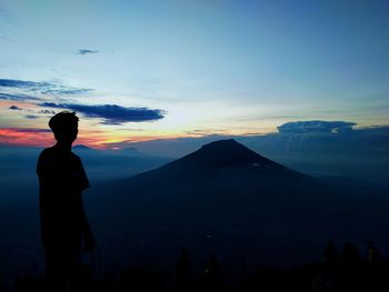 Rear view of silhouette man standing on mountain against sky