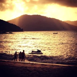 Silhouette people on beach against sky during sunset