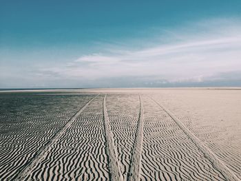 Tire tracks on sand pattern against sky at beach