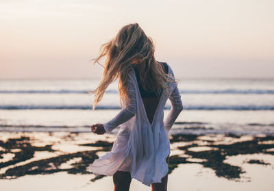 Rear view of woman at beach against clear sky during sunset