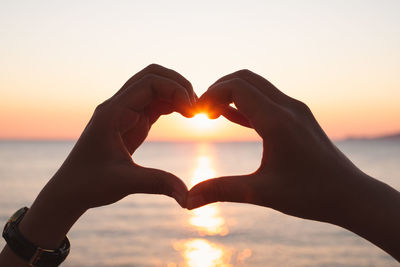 Close-up of hands making heart shape against sky during sunset