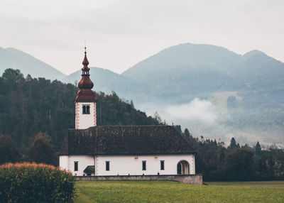 Built structure by trees and mountains against sky