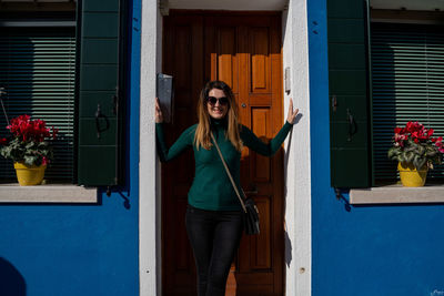 Portrait of young woman standing against door