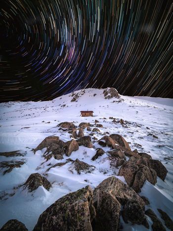 Star trails over snow covered landscape at night