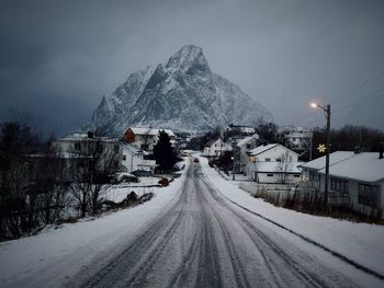 Snow covered road by buildings against sky