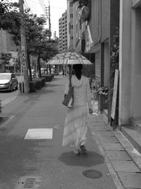 Rear view of woman with umbrella walking on footpath