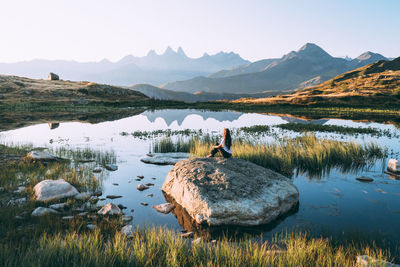 Rear view of woman sitting on rock in lake against sky