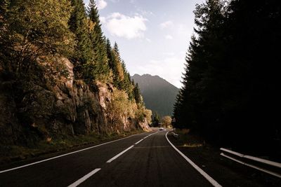Road amidst trees and mountains against sky