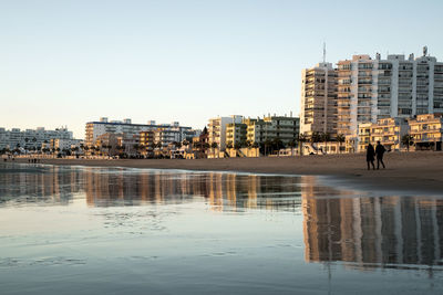 Reflection of buildings in river against clear sky