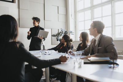 Businessman holding laptop and explaining colleagues in meeting at office