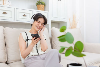 Young woman using mobile phone while sitting on bed at home