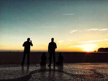 Silhouette people on beach against sky during sunset