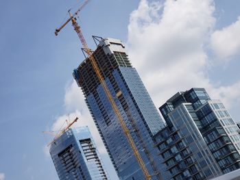 Low angle view of crane by building against sky
