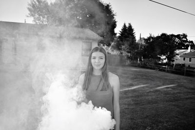 Portrait of young woman standing amidst smoke at yard
