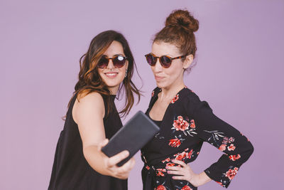 Women taking selfie with mobile phone against wall