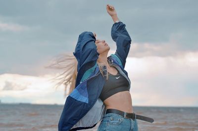 Woman with arms raised at beach against sky