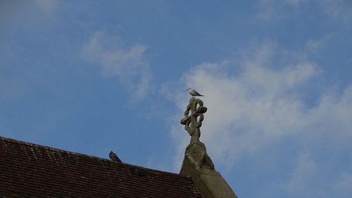 Low angle view of statue on building roof against sky