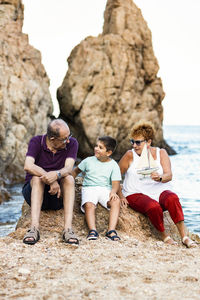 Grandparents and grandson playing with a toy sailboat on the beach