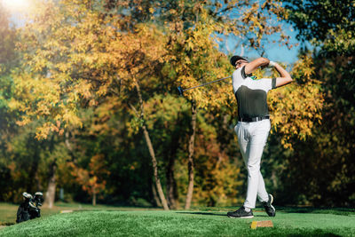 Young golfer on the tee box, hitting the ball with the driver club on a sunny autumn day