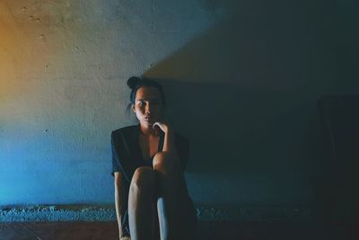 Portrait of young woman sitting against wall in darkroom