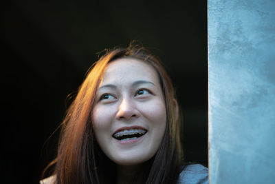 Close-up of young woman looking away while standing by wall