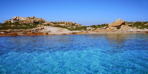 Rock formations in sea against clear blue sky