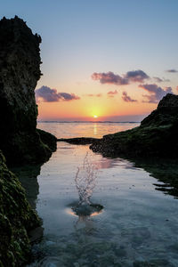 Water splashing in sea against sky during sunset