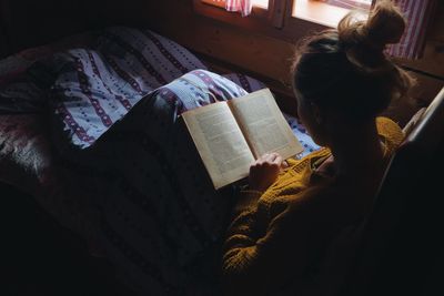 Young woman reading book on bed at home