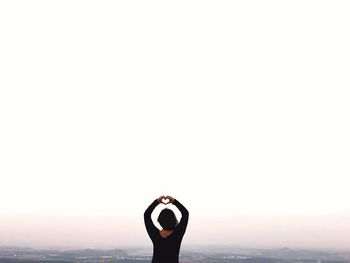 Rear view of woman making heart shape against clear sky