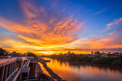 Scenic view of river by buildings against sky during sunset