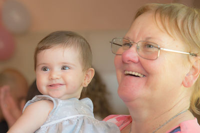 Close-up of cheerful grandmother holding granddaughter at home