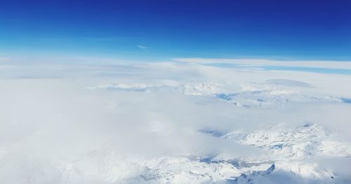 Aerial view of snowcapped mountains against blue sky