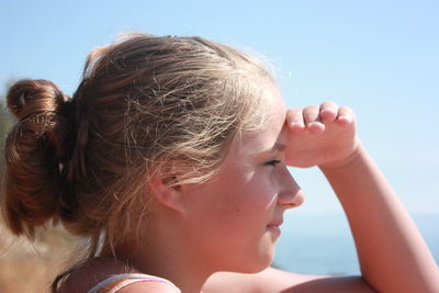 Side view of smiling young woman shielding eyes during sunny day