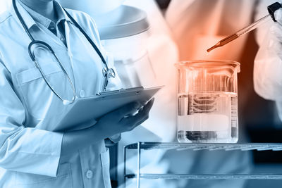 Double exposure of female doctor holding clipboard with chemicals in laboratory