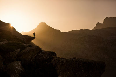 Back view of unrecognizable female traveler silhouette sitting on edge of cliff and admiring picturesque mountains in morning in pyrenees