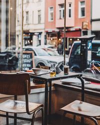 Empty chairs and tables at sidewalk cafe in city