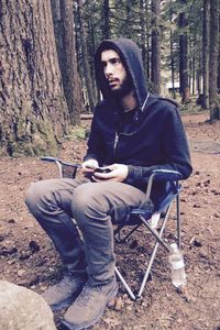 Portrait of young man sitting on tree trunk in forest