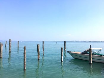 Wooden posts and boat moored in sea against sky