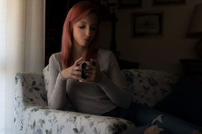 Young woman holding mug while sitting on sofa at home