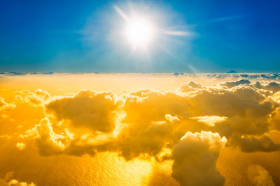Airplane view of landscape with clouds, ocean with mountain peak and bright sunset shining sun