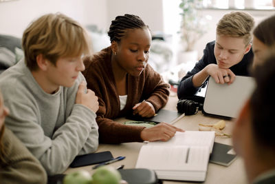 Teenage girls and boys studying together at table in living room