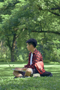 Young man sitting on land against trees