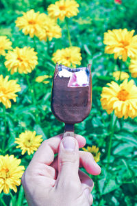 Cropped hand holding ice cream against yellow flowers on field