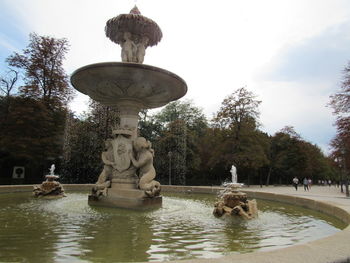 Statue by fountain in park against sky